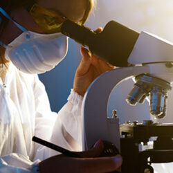 Woman wearing mask looking through microscope